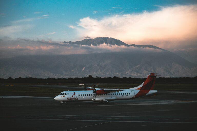 Avianca aircraft parked on tarmac with majestic mountains in the backdrop under a dramatic sky.